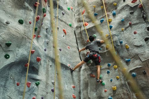 Free Back view of faceless man in sportswear with belay performing extreme climbing on wall during workout Stock Photo