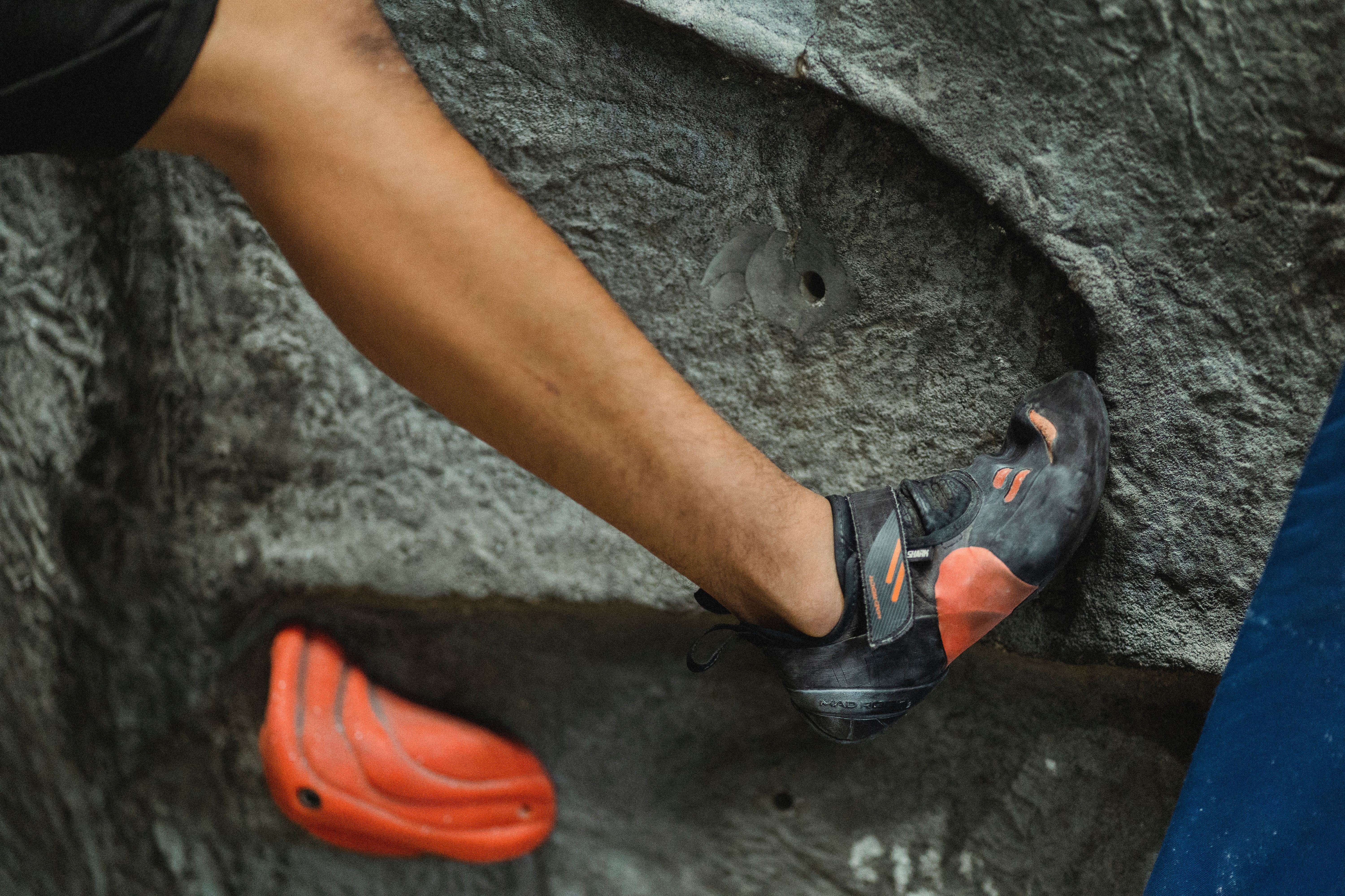 Crop unrecognizable male alpinist in sport sneakers practicing bouldering in modern climbing center