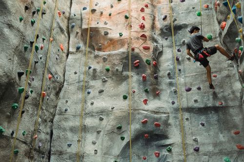Free Full body of faceless male climber in sportswear hanging on rope while exercising on climbing wall Stock Photo