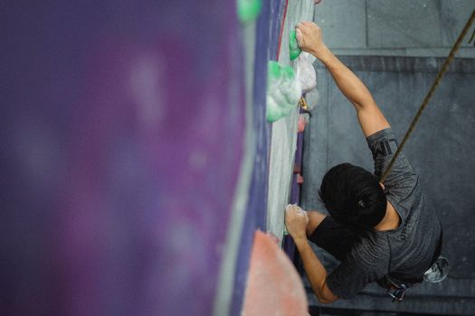 From above of faceless male athlete with belay climbing on wall in bouldering center
