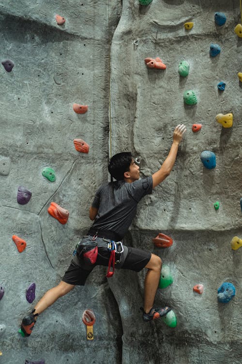 Concentrated male mountaineer in sportswear training on climbing wall in modern bouldering center