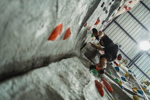 Low angle of unrecognizable male climber in activewear performing bouldering training with belay