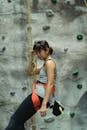 Side view of active female alpinist in sportswear hanging on belay while practicing climbing in gym