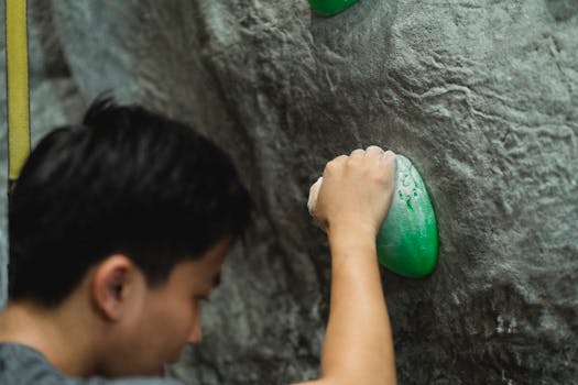 Faceless male mountaineer with hands in talc practicing bouldering on climbing wall in modern gym