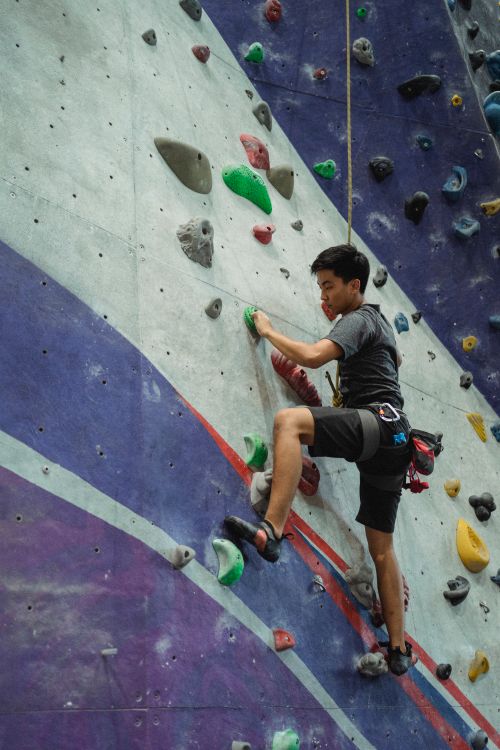 Free Full length of strong ethnic male athlete in sportswear with belay clambering high in bouldering center Stock Photo