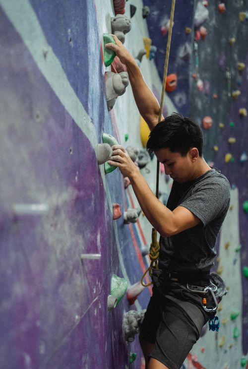 Free Side view of male mountaineer with belay training on climbing wall in gym Stock Photo