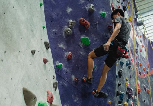 Low angle of unrecognizable male athlete in sportswear hanging on rope after performing exercise on climbing wall