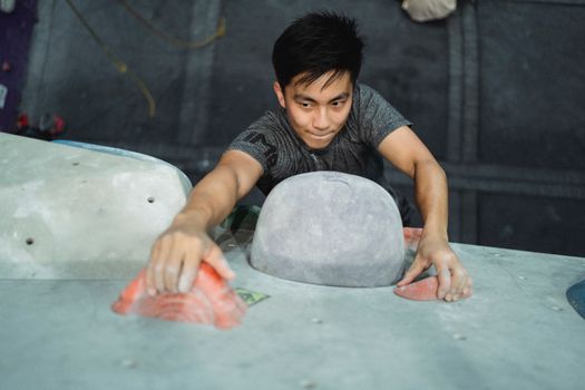 Strong Asian man clambering wall in gym