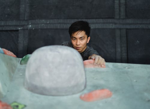 Free Focused Asian male athlete in gray sportive t-shirt climbing on climbing wall and looking forward Stock Photo