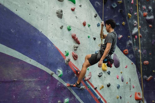 Free Side view of unrecognizable male athlete in sportswear hanging on rope during bouldering workout in gym Stock Photo