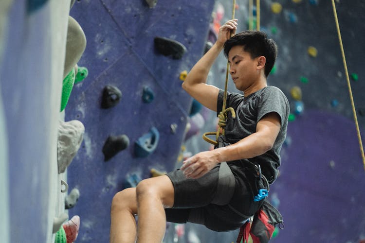 Asian Man Hanging On Belay After Bouldering