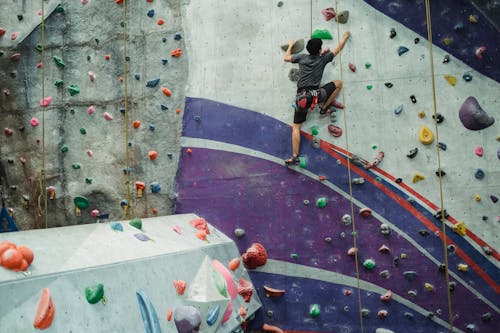 Free Back view of unrecognizable male athlete with belay training on climbing wall in bouldering center Stock Photo