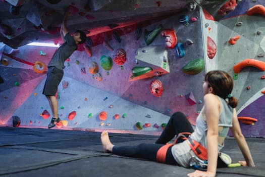 Two individuals engage in indoor rock climbing at a gym, showcasing strength and teamwork.
