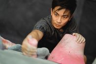 Young Asian guy ascending on climber wall in gym