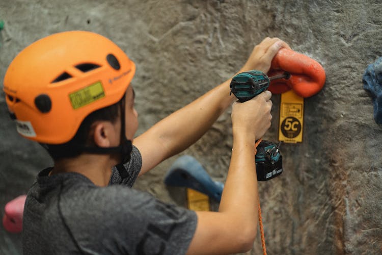 Crop Athlete Fasten Climbing Hold With Screwdriver On Wall In Gym