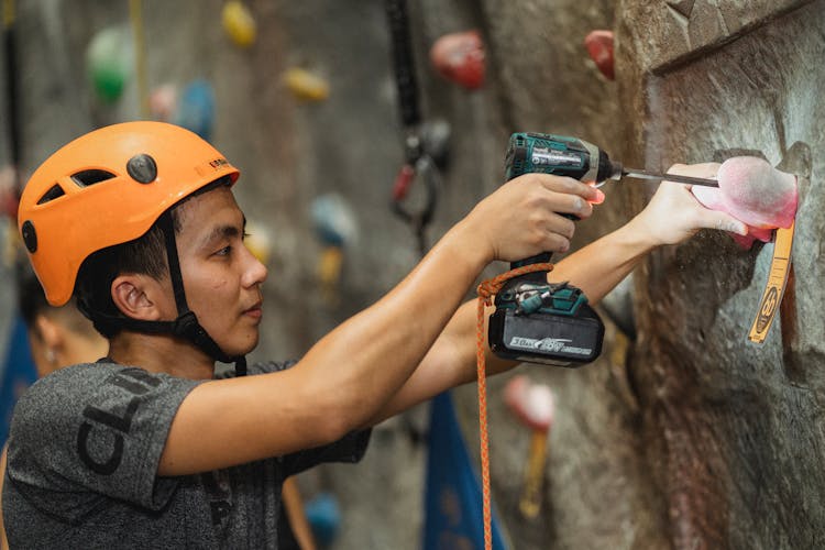 Young Asian Specialist Drilling Pink Climbing Hold On Wall In Gym