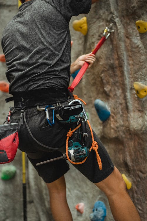 Unrecognizable male technician hanging on safety rope near climbing wall