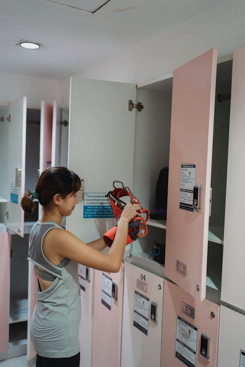 Asian lady getting safety strap from opened locker in gym