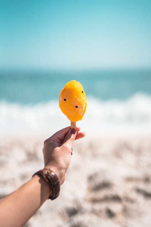 Shallow Focus Photo of Person Holding a Yellow Popsicle