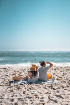 Couple enjoying a summer picnic on the beach with a stunning ocean view.