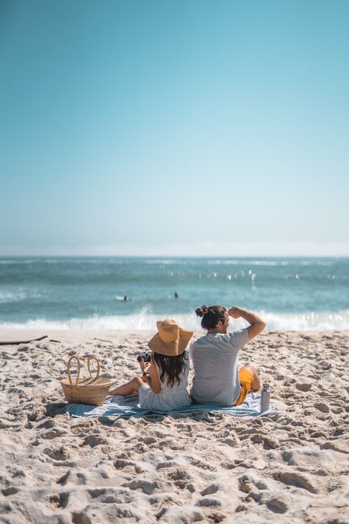 Free Couple enjoying a summer picnic on the beach with a stunning ocean view. Stock Photo