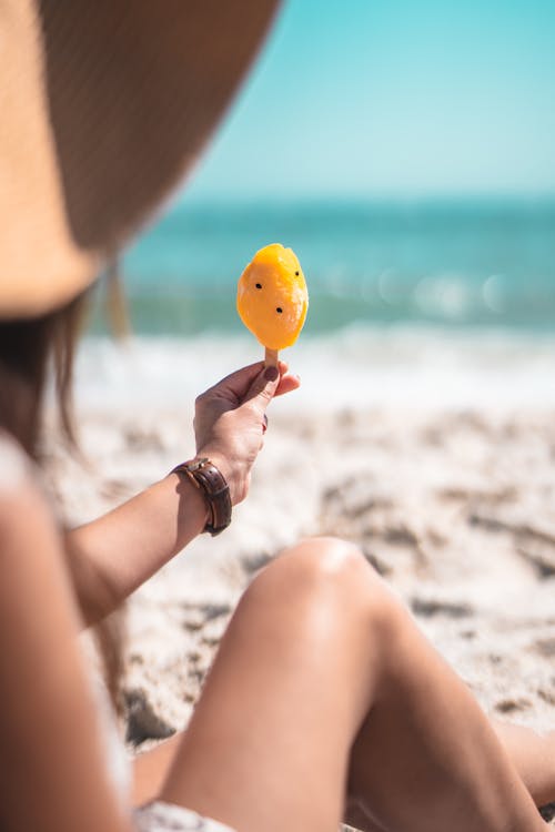 Shallow Focus Photo of Person Holding a Yellow Popsicle