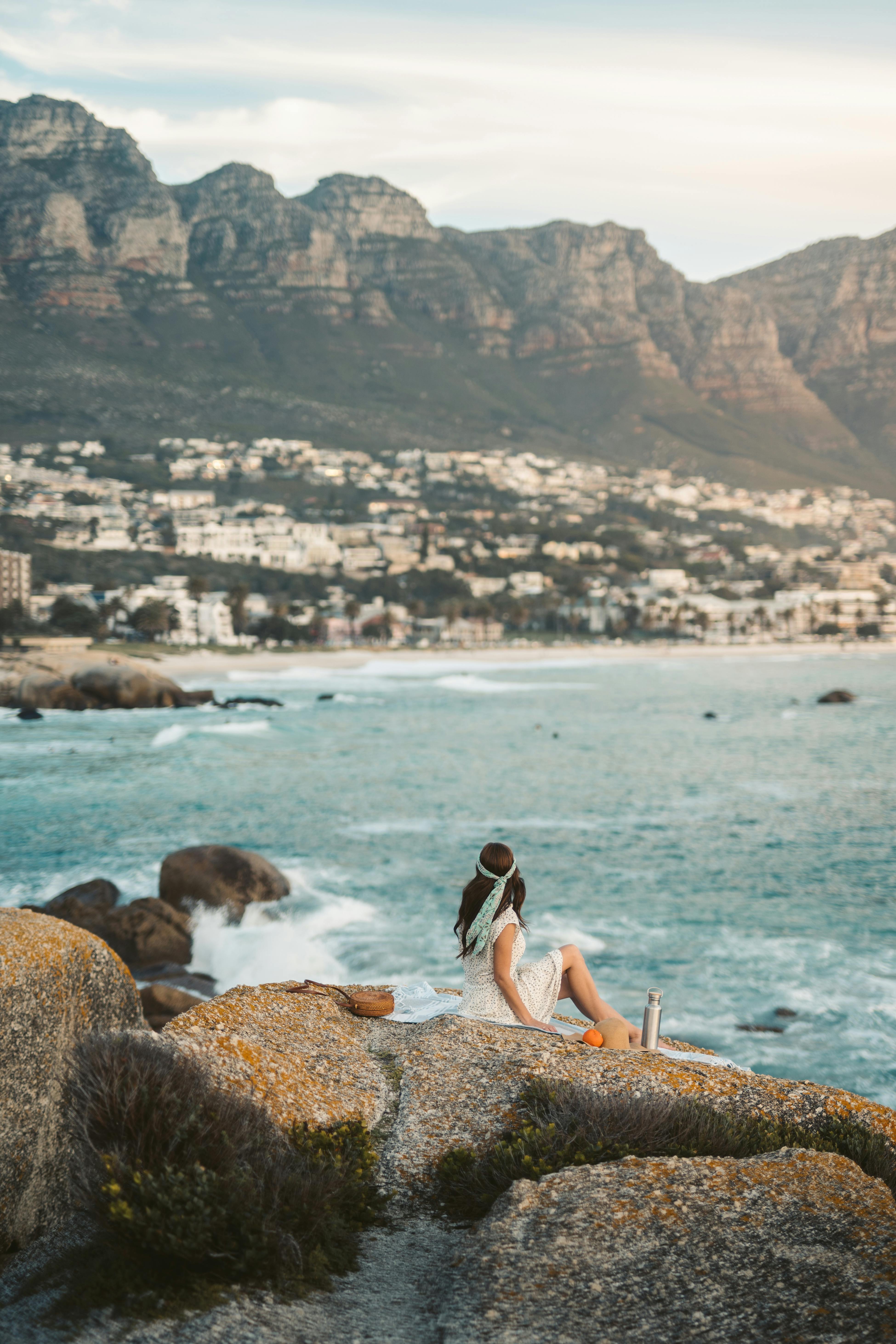 一名妇女坐在岩石上，以山区为背景，俯瞰开普敦海岸线的宁静景色
