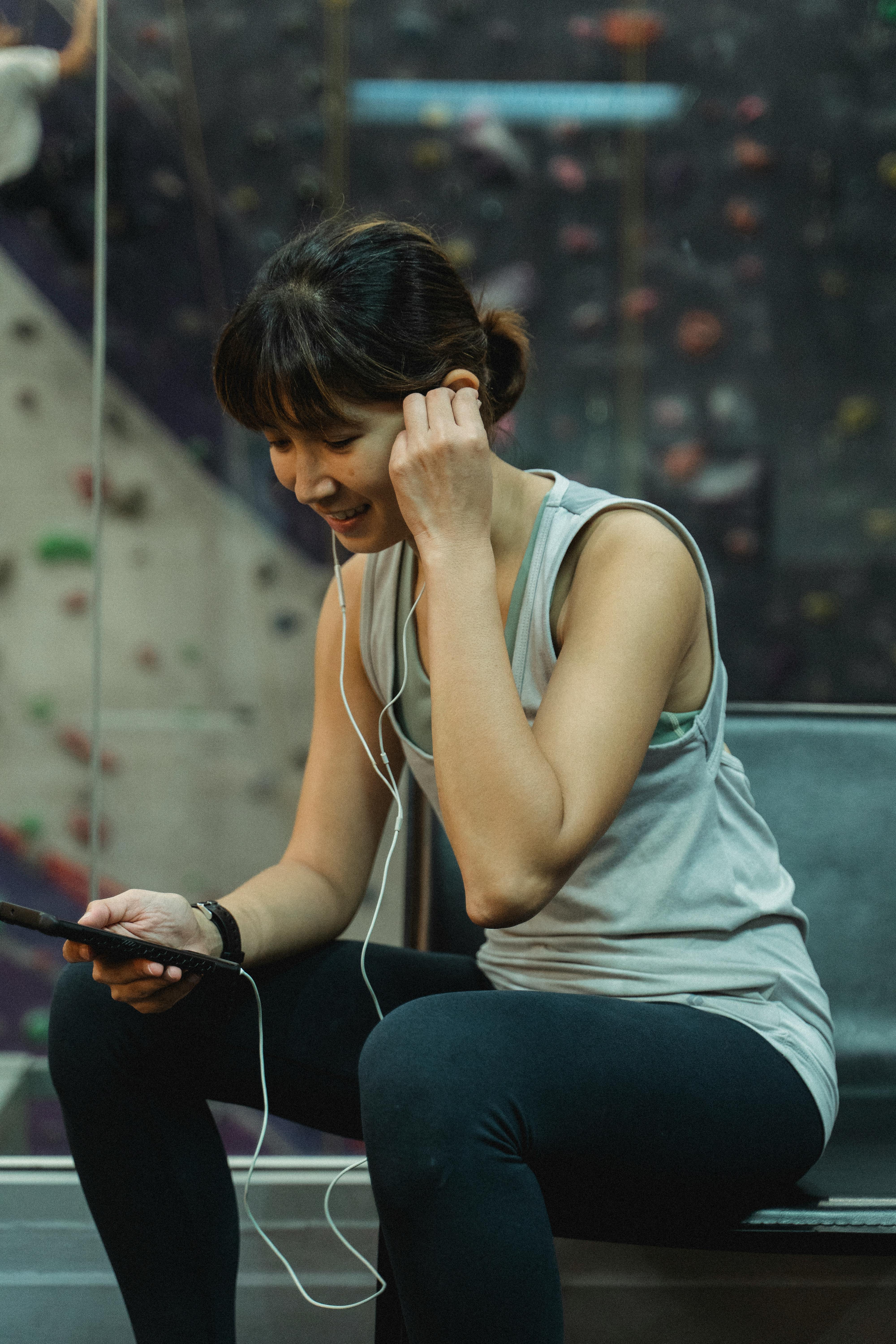 smiling young ethnic sportswoman in earphones having video chat in gym