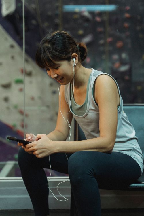 Free Side view of young Asian sportswoman in earphones and activewear smiling while listening to music via smartphone after training in modern climbing gym Stock Photo