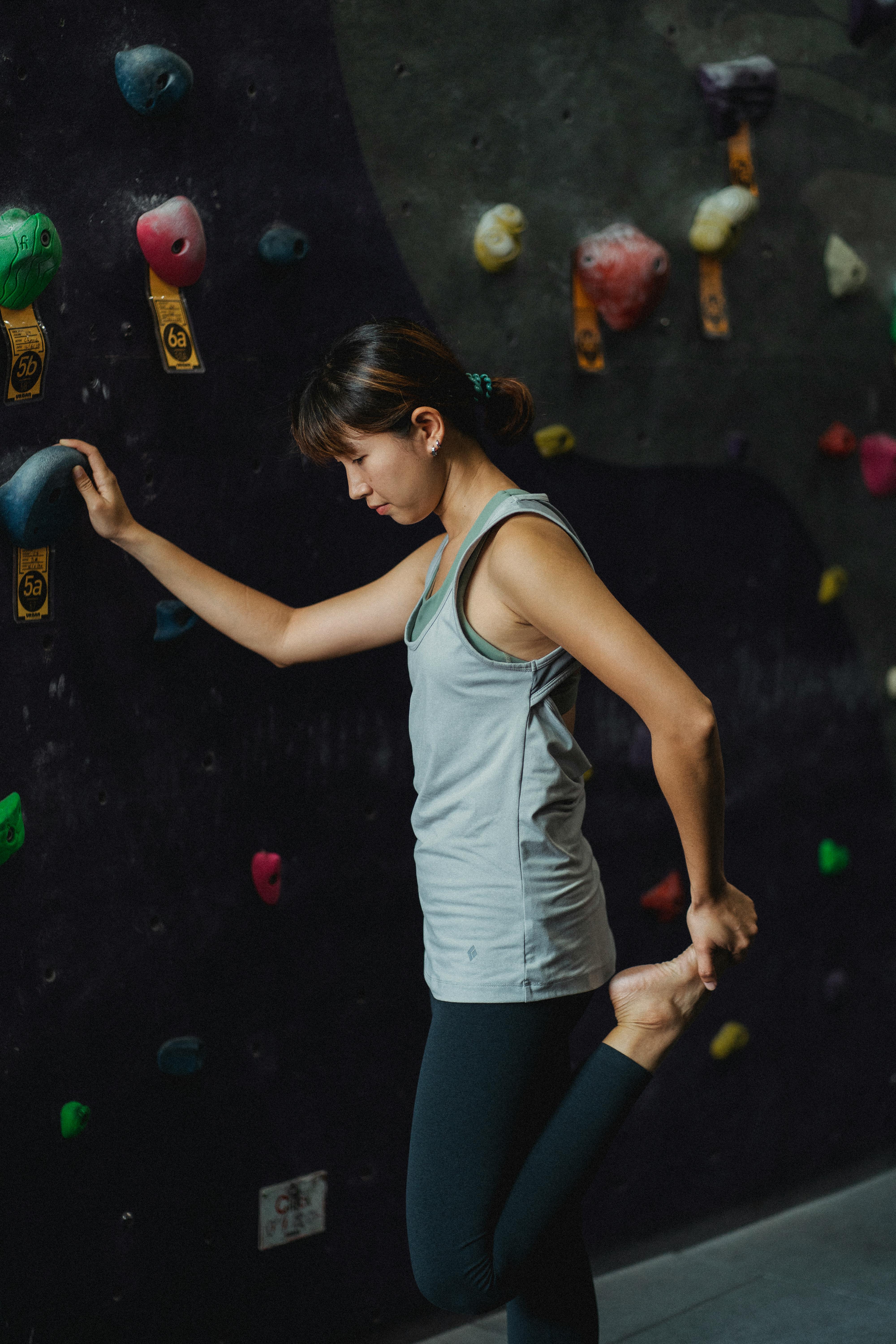 Slim young Asian sportswoman stretching legs before climbing wall