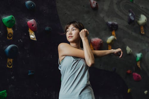 Free Low angle of determined young Asian sportswoman in activewear stretching arms while warming up before ascending climbing wall in gym Stock Photo
