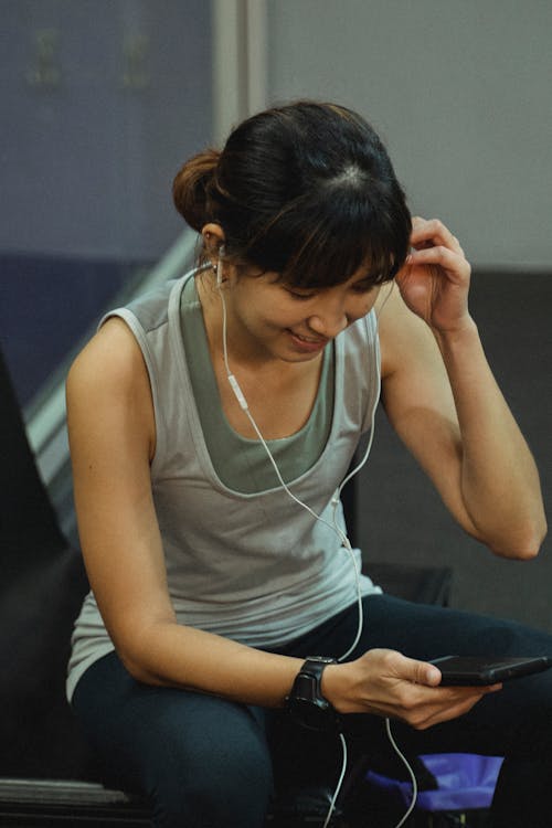 Delighted young ethnic lady chatting on smartphone in earphones after training