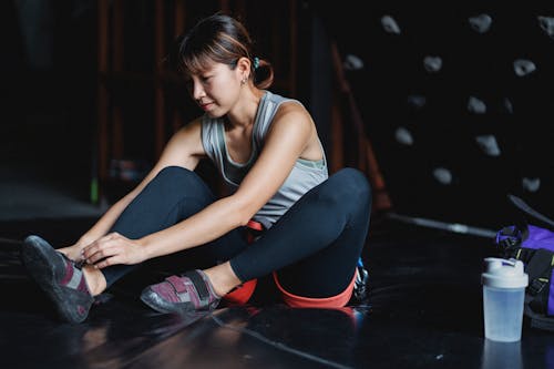 Young Asian sportswoman wearing sneakers sitting on mat in climbing club