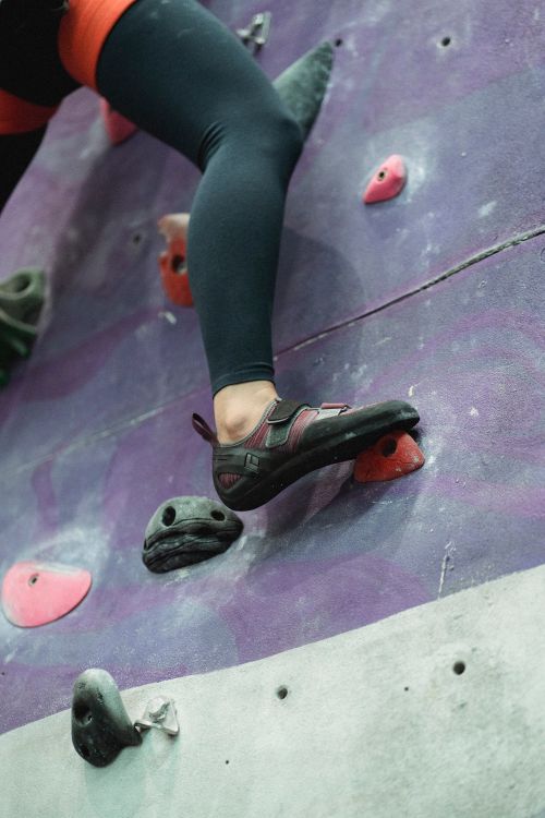 Free From below of crop unrecognizable female alpinist in sportswear and safety harness practicing climbing on artificial rock wall in gym Stock Photo