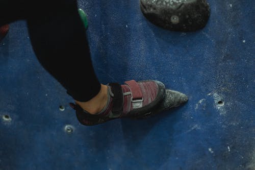 Crop unrecognizable female mountaineer putting leg on grip while ascending climbing wall in gym