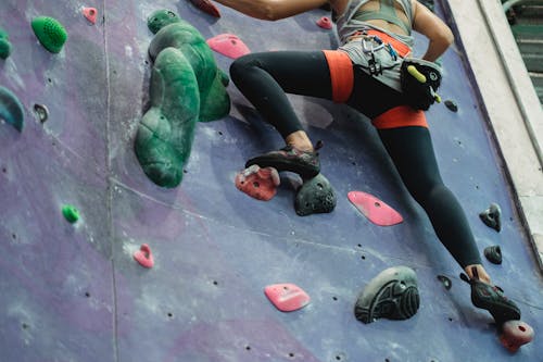 Low angle of crop unrecognizable sportswoman in activewear and safety harness ascending wall while training in climbing gym