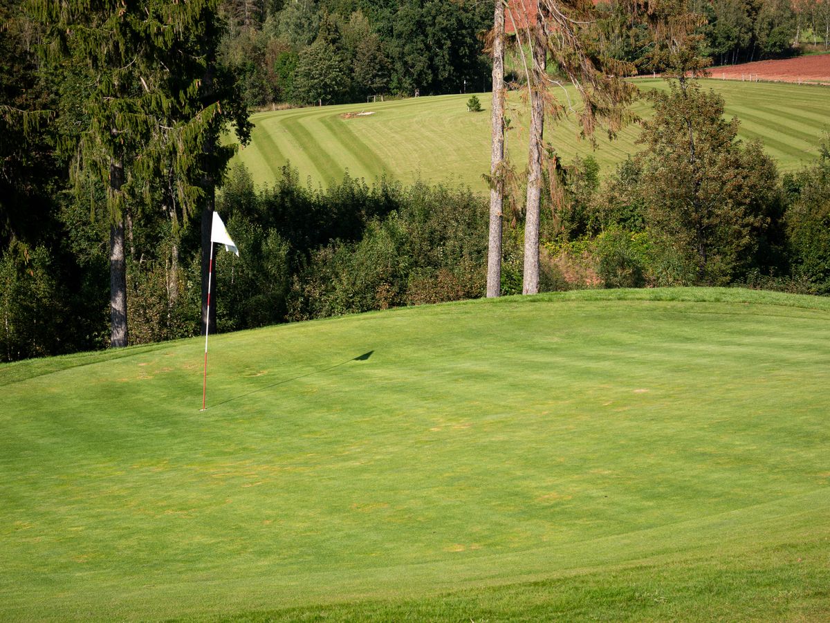 Green golf course fairway with a flagstick under clear skies