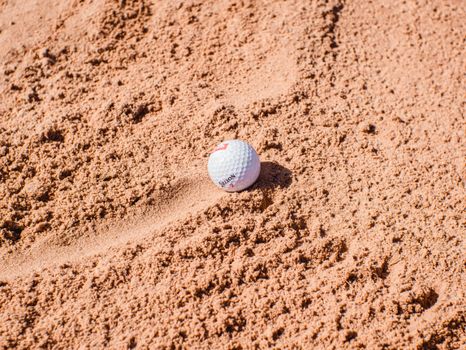 Close-up of a golf ball on a sand trap, highlighting texture and challenges of the sport.