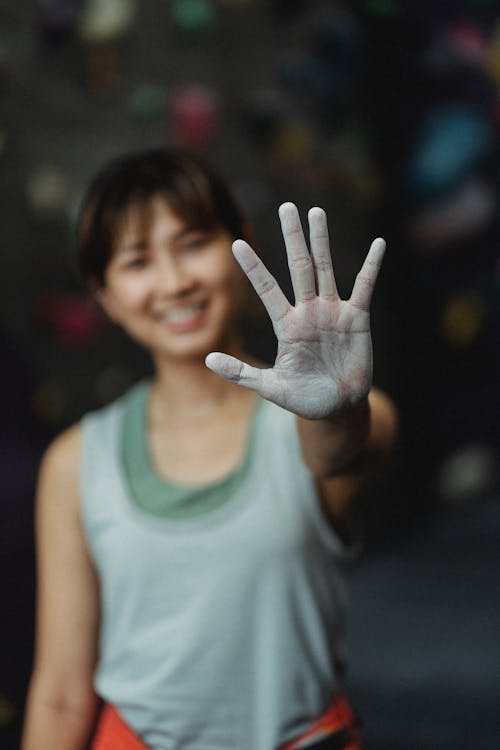 Cheerful young ethnic female climber smiling and showing white chalked hand before training in gym