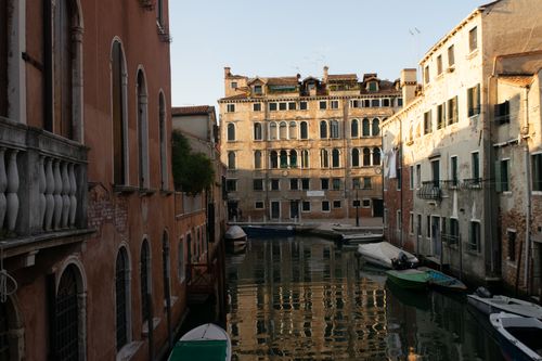 Free Beautiful view of a narrow Venetian canal with historic buildings and moored boats at sunset. Stock Photo