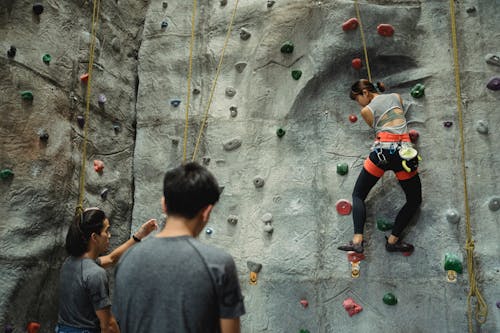 Free Anonymous female boulderer practicing climbing with male instructors in gym Stock Photo