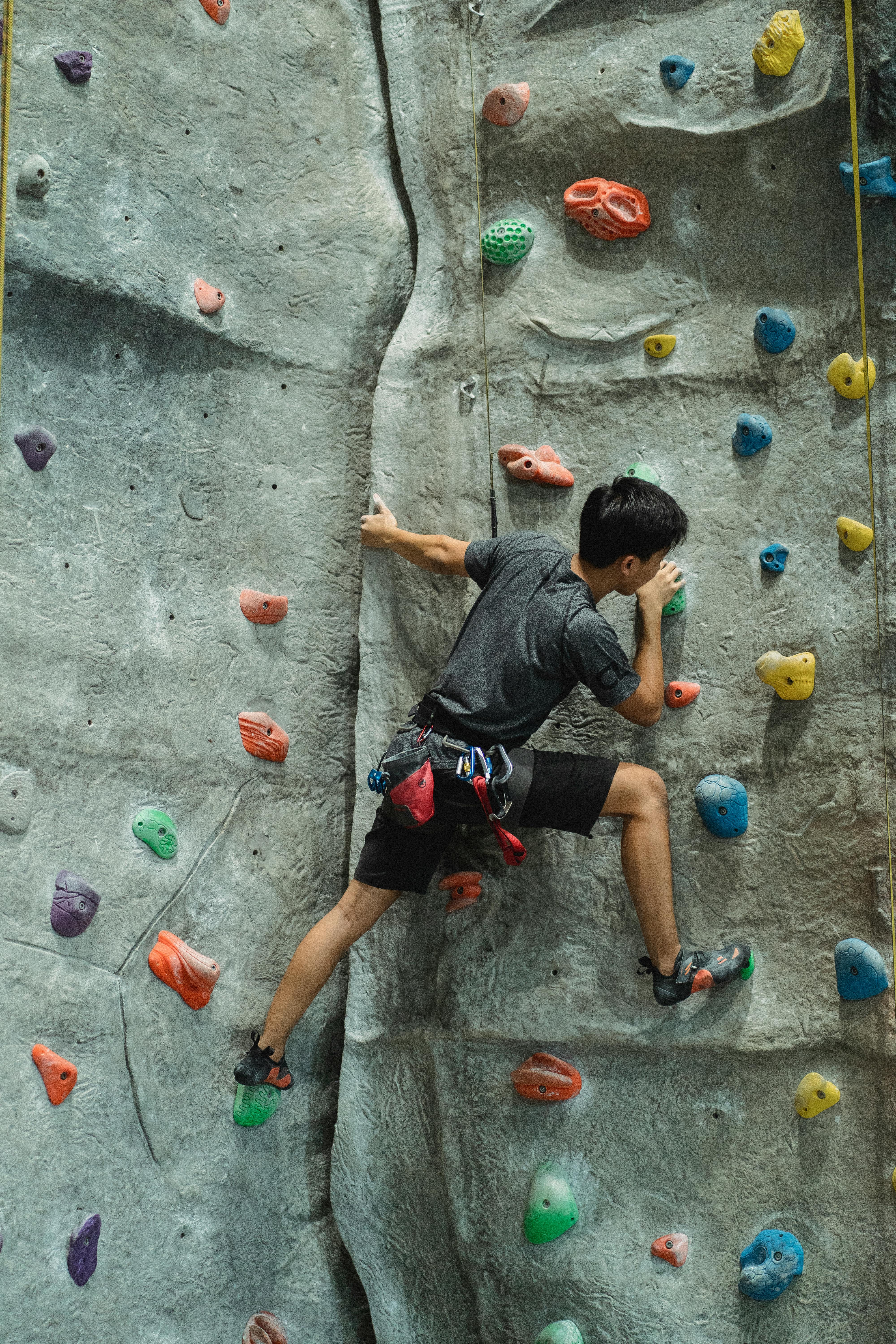 unrecognizable male boulderer climbing wall in gym