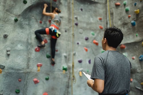 Anonymous male trainer controlling female climber ascending wall