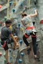 From below back view of young Asian male mountaineer with unrecognizable sportswoman climbing wall with grips while practicing extreme sport