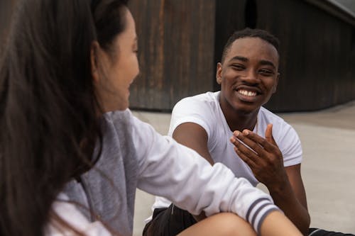 Cheerful young African American guy in casual clothes smiling while chilling on street with crop Asian female friend