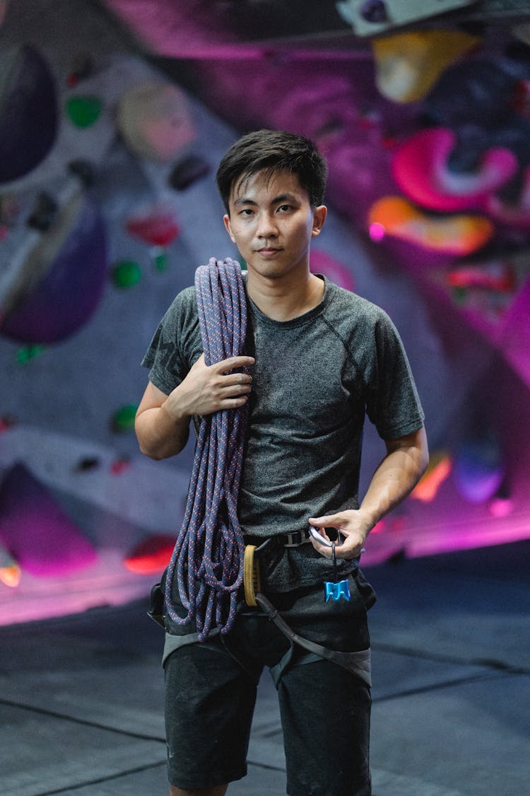 Asian Sportsman With Dynamic Rope Against Climbing Wall