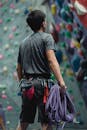 Back view of anonymous fit mountaineer in sportswear with dynamic rope looking up against artificial rock