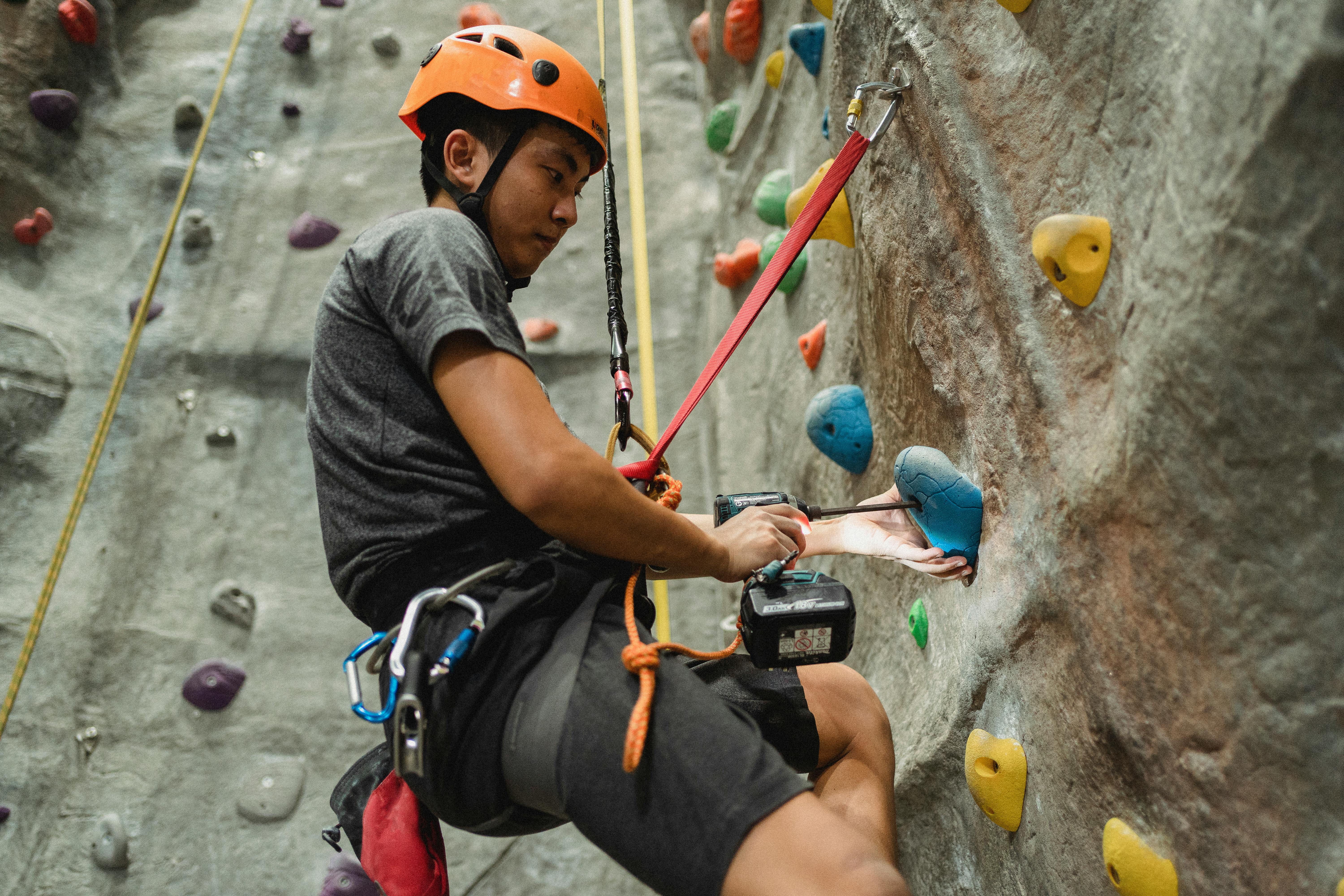 ethnic male alpinist fixing grip on climbing wall