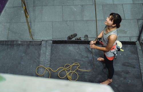From above of young glad barefoot ethnic sportswoman in active wear with safety equipment looking up before training