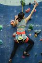 Back view of unrecognizable slim female mountaineer in sportswear with harness climbing artificial rock with grips